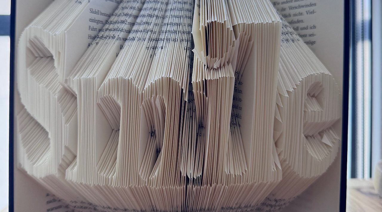 Hardcover Buch in dessen Seiten das Wort „Smile“ gefaltet wurde.