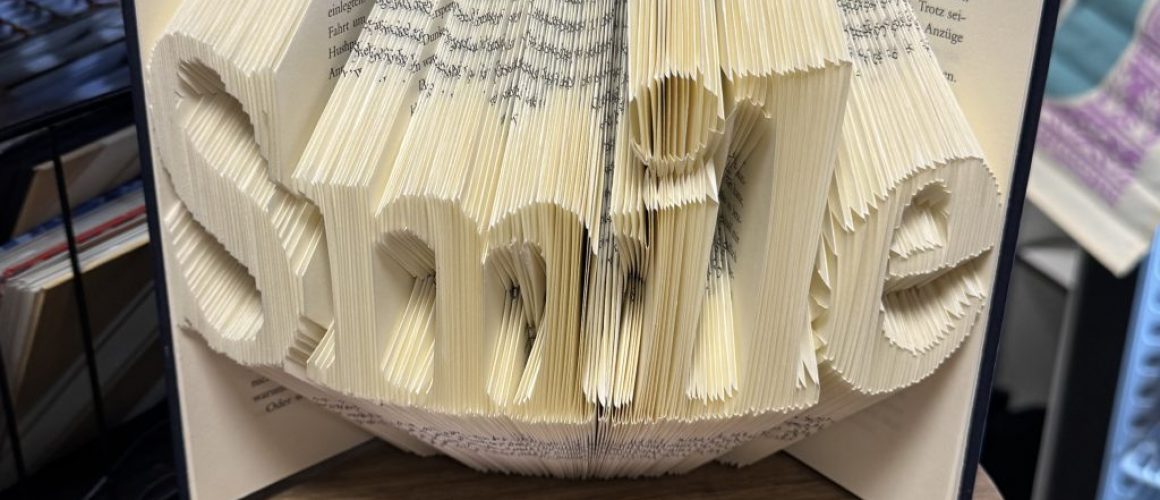 Hardcover Buch in dessen Seiten das Wort „Smile“ gefaltet wurde.