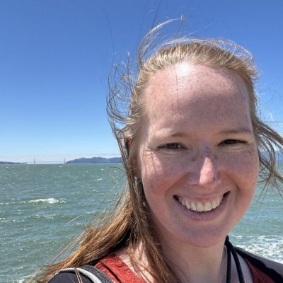 Lächelnde Frau mit rot-braunen, mittellangen Haaren vor der San Francisco Bay mit Golden Gate Bridge im Hintergrund